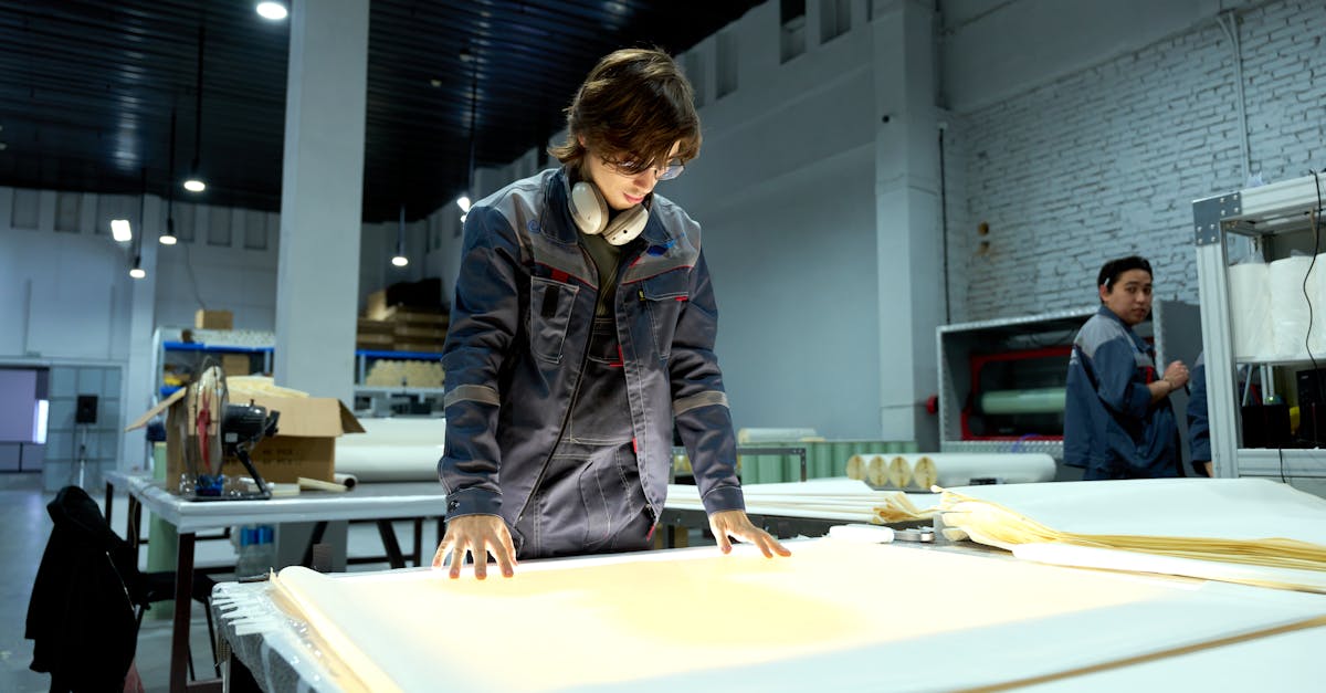 Worker in uniform examining sheets in a brightly lit factory environment, focusing on quality.