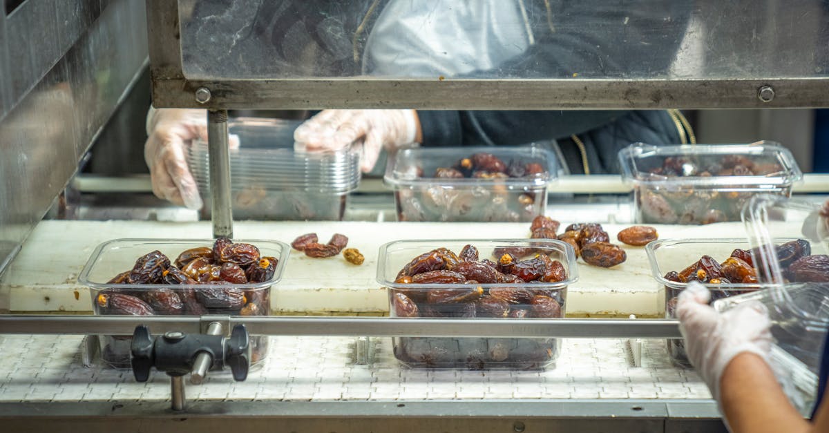 Close-up image of workers packing dates with gloves in a factory setting.