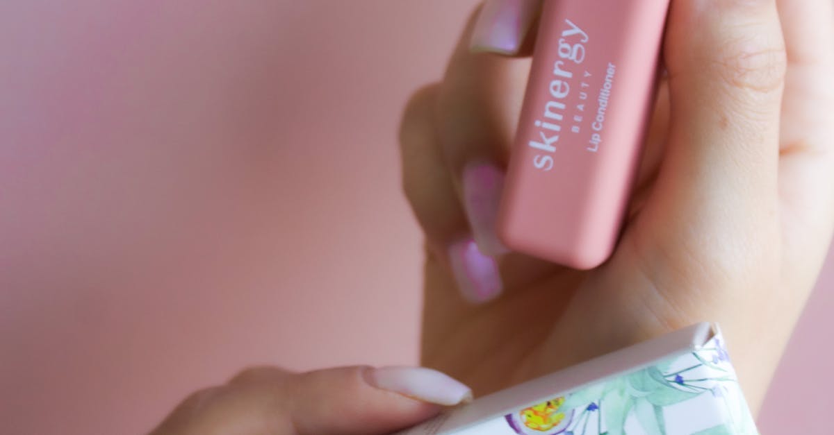 Close-up of hands holding pink cosmetic product and packaging, on a pastel background.