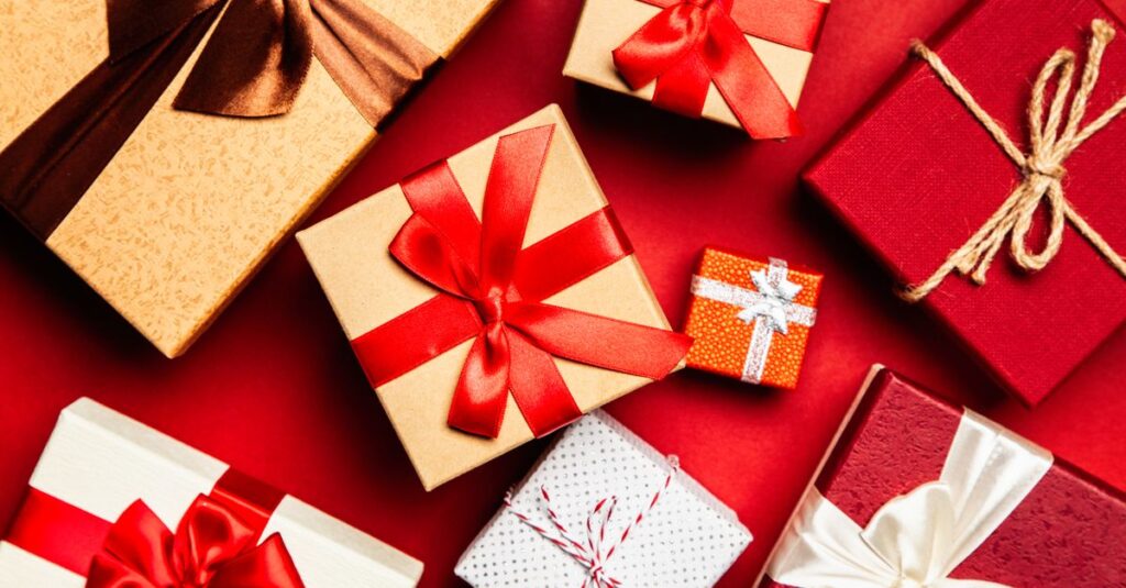 Top view of beautifully wrapped holiday gifts with red and brown ribbons on a vibrant red background.