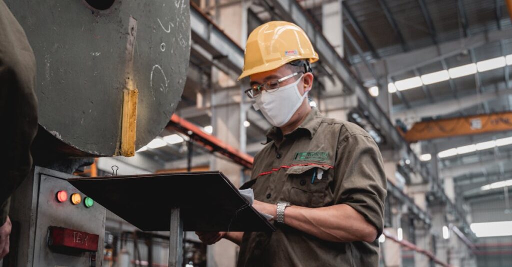 Factory worker with safety gear checks machinery, ensuring industrial safety compliance.