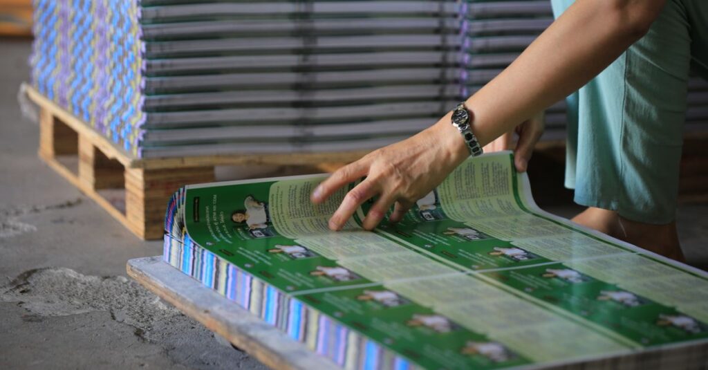 A person organizes stacks of printed publications in an industrial warehouse setting.