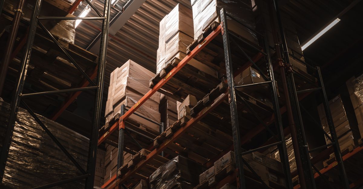 Interior view of a warehouse with stacked cardboard boxes on high shelves, showcasing storage and logistics.