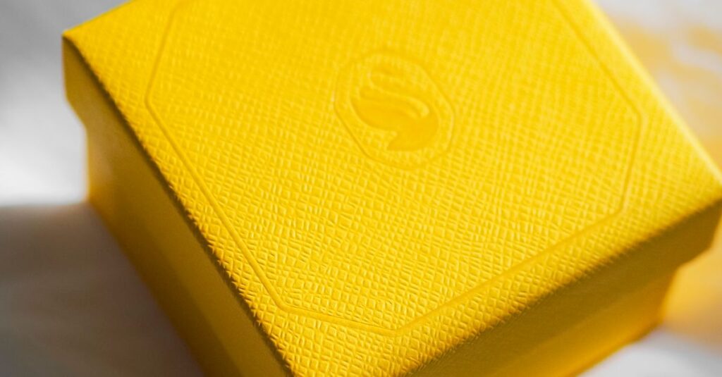 Bright yellow gift box on white fabric with sunlight highlighting its texture.