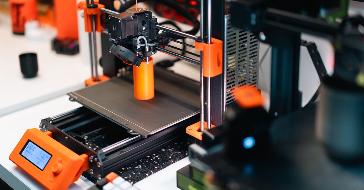3D printer operating in a workshop, creating a prototype with orange accents.