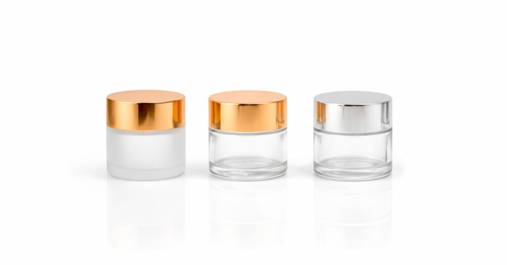 Stylish glass cosmetic jars with metallic lids on a white background, perfect for beauty packaging concepts.