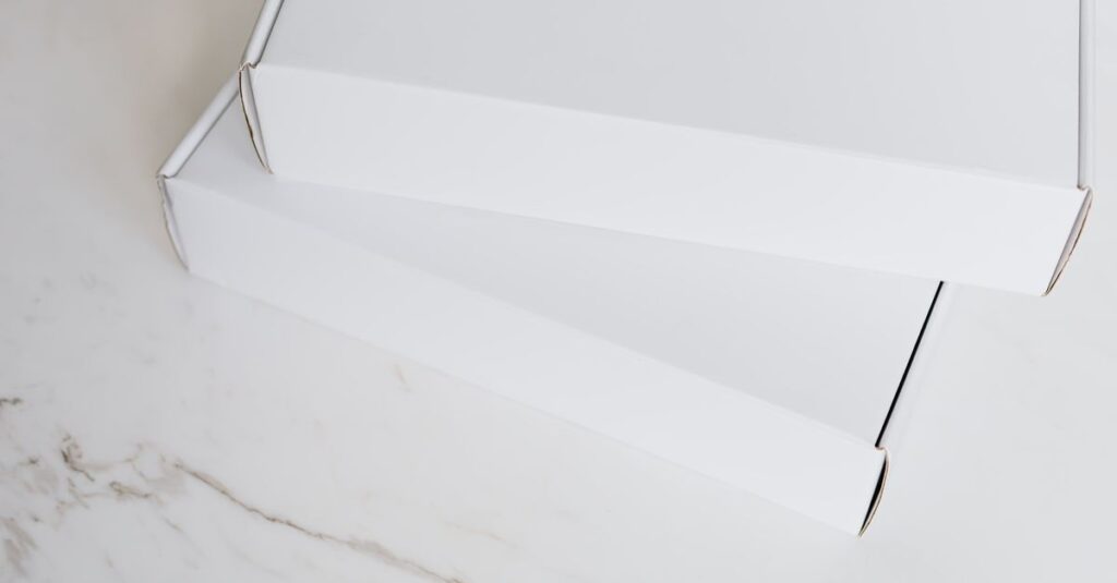From above of pair of closed white cardboard boxes for postal or courier delivery arranged on white marble tabletop for sending preparation