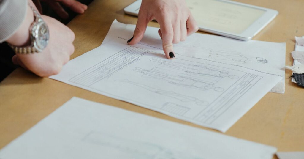 Two fashion designers review clothing sketches in a creative workspace, focusing on design plans.
