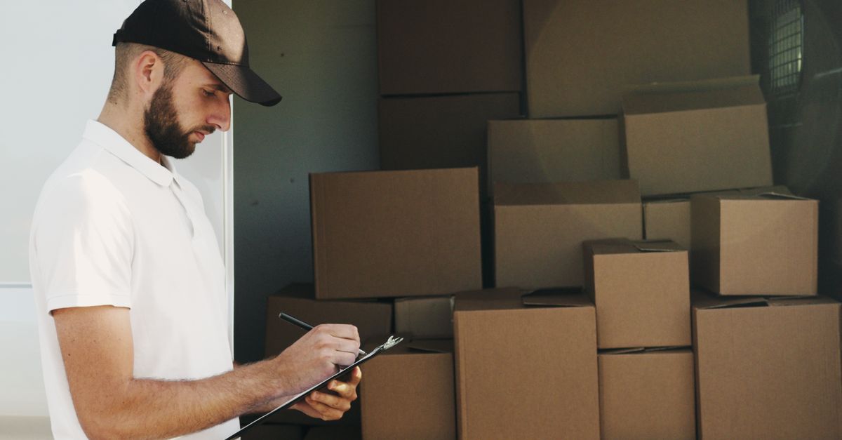 Deliveryman writing on clipboard next to stacked cardboard boxes in a van.