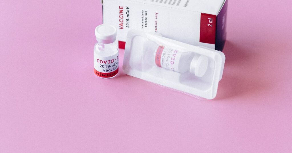 A COVID-19 vaccine vial with packaging on a pink background, representing health and vaccination.