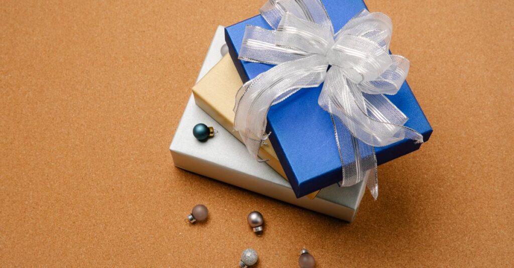 From above wrapped blue Christmas gift box decorated with organza ribbon on top of stack of boxes and small baubles beside