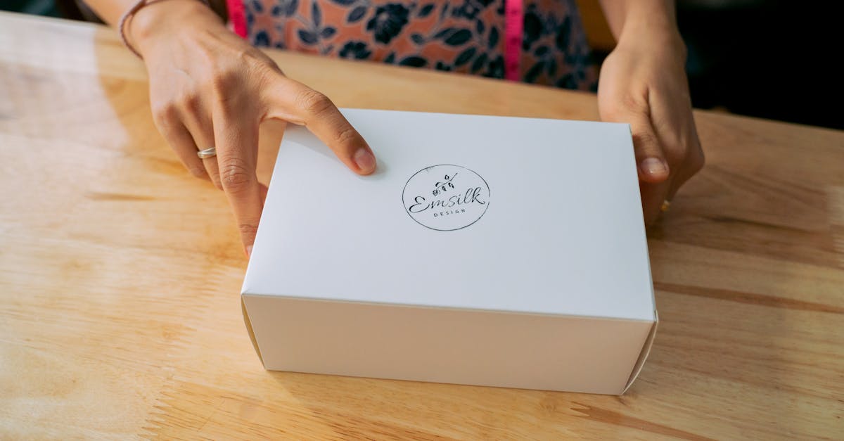 Close-up of hands holding a white branded box on a wooden table.