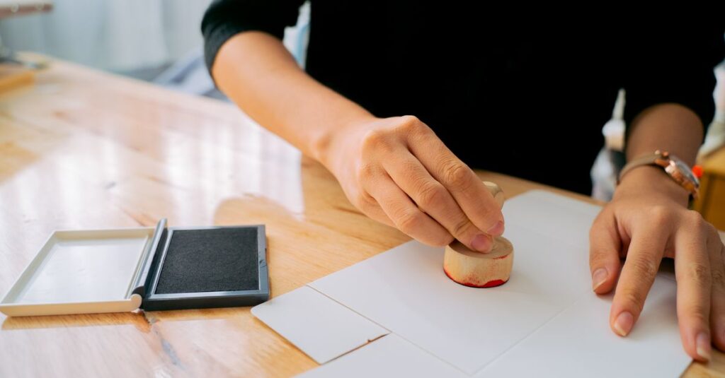 Close-up of hands stamping a document on a wooden desk indoors.