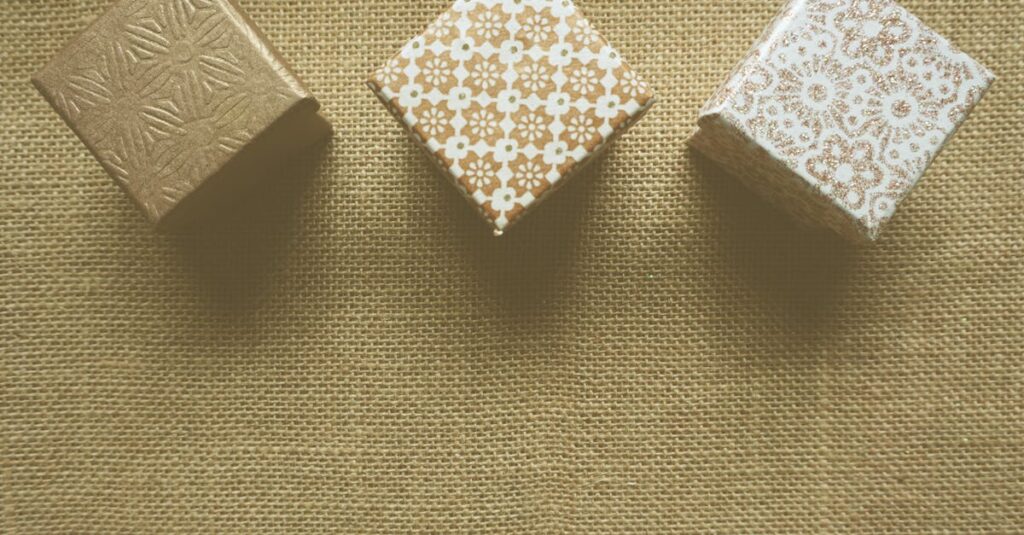 Three decorative gift boxes on a textured burlap surface creating a warm and rustic look.