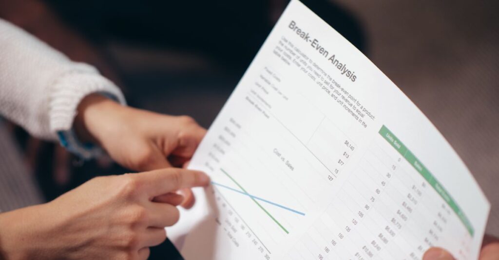 Close-up of hands discussing a break-even analysis document in a business meeting.