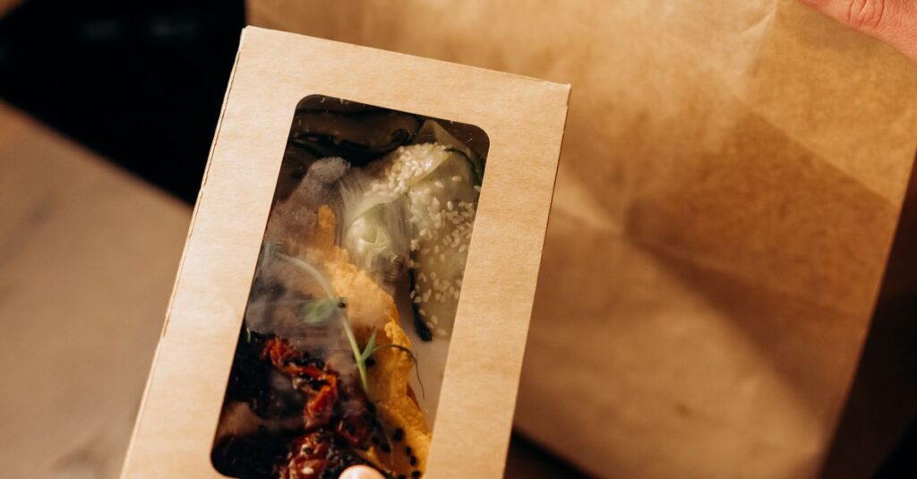 Hands holding a cardboard food container next to a paper bag, suggesting eco-friendly delivery.