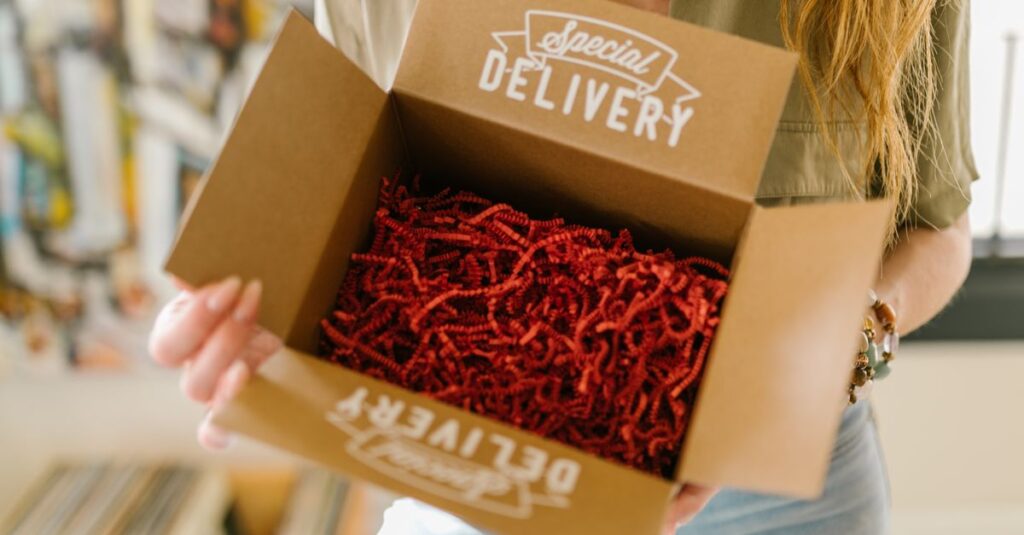 Person opening a special delivery box filled with red crinkle paper for secure packaging.