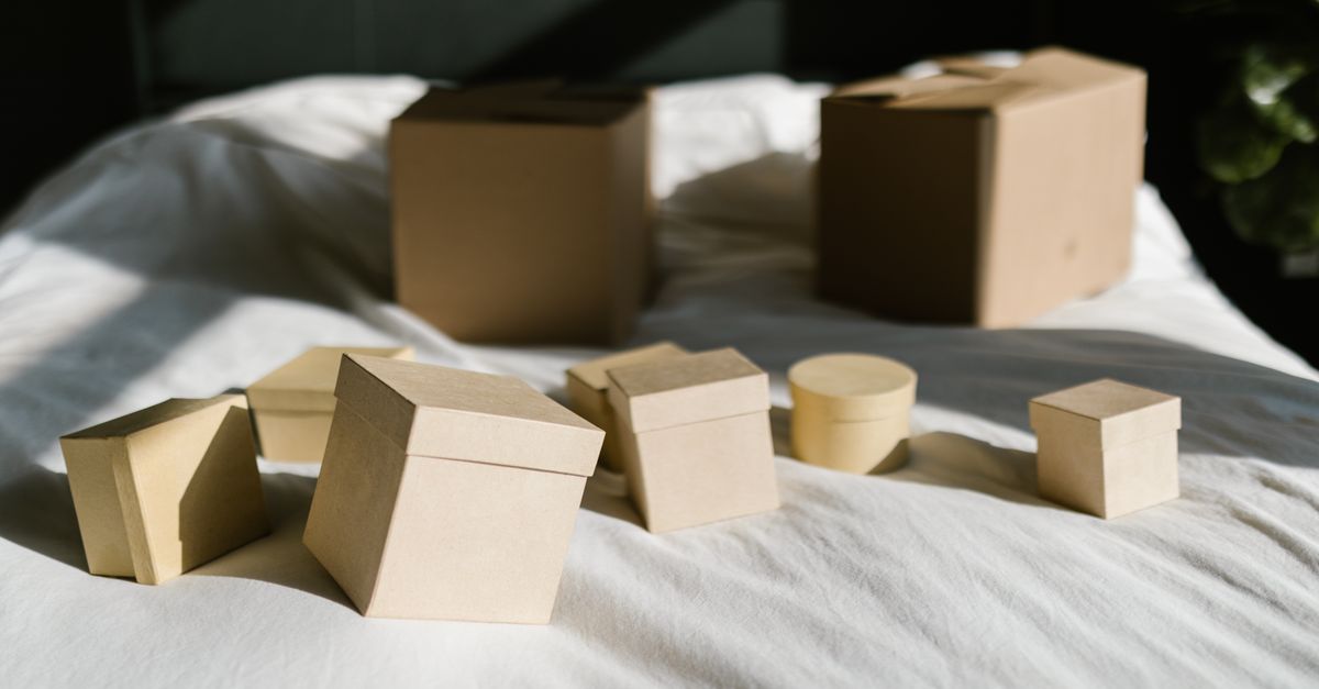 Cardboard boxes with lids arranged on a sunlit bed, casting shadows.