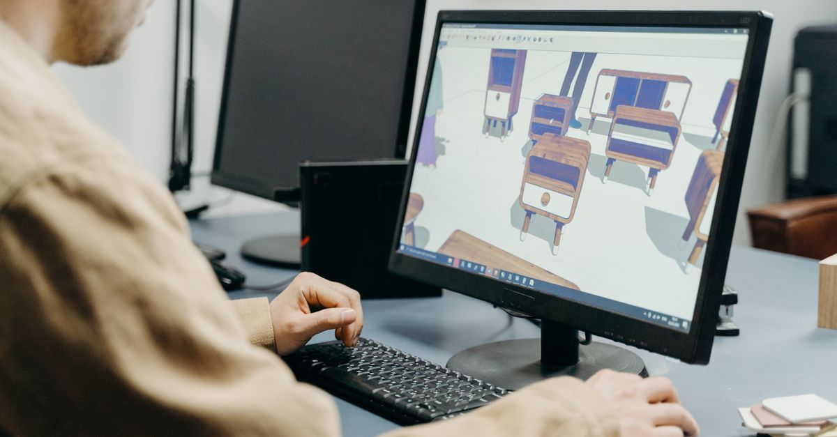 A product designer using a computer for 3D furniture modeling in an office setting.