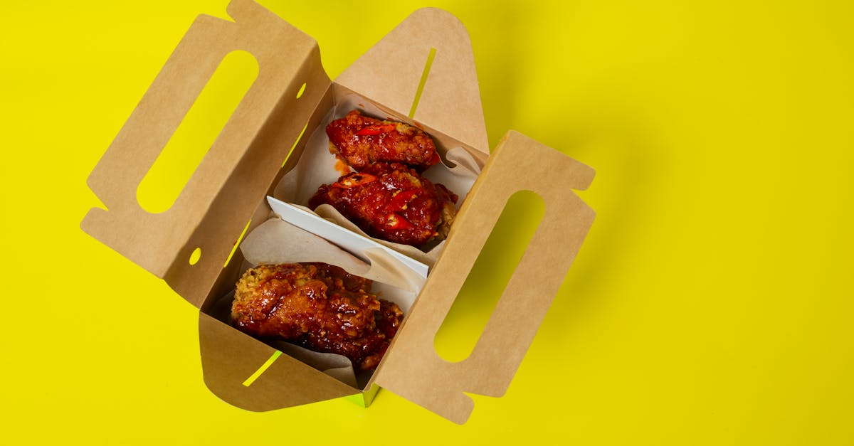 Savor spicy fried chicken wings in a box on a vibrant yellow background, perfect for food photography.