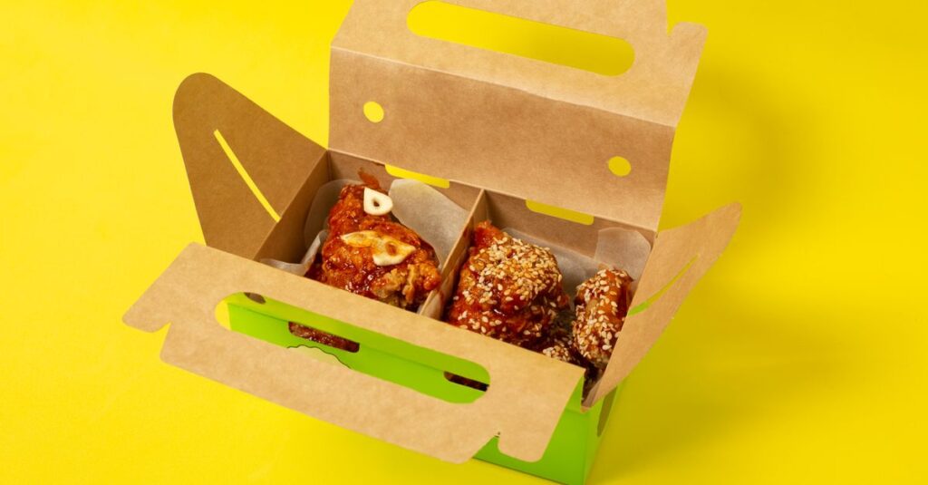 From above of appetizing chicken meat with garlic placed in cardboard box on yellow background in studio