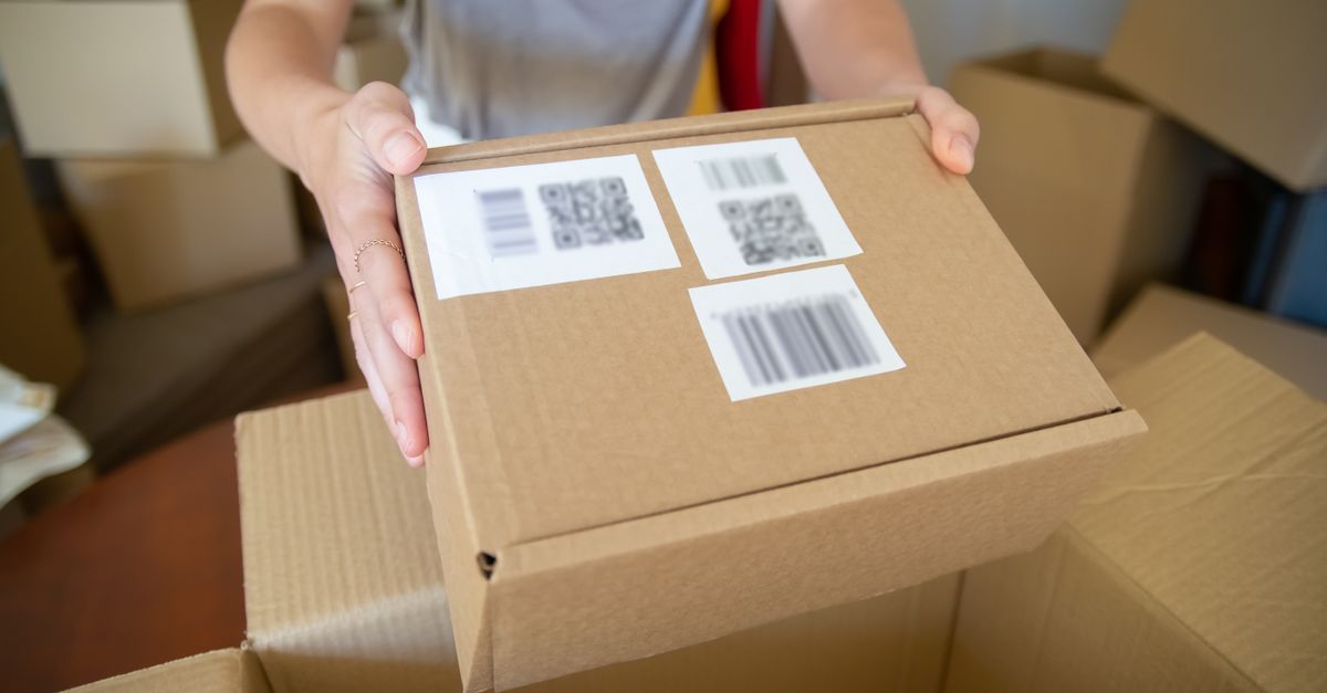 Close-up of a person holding a cardboard box with barcode labels, indoors setting.