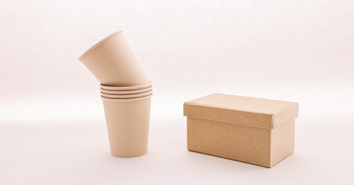 A stack of eco-friendly cardboard cups next to a closed box on a white background.