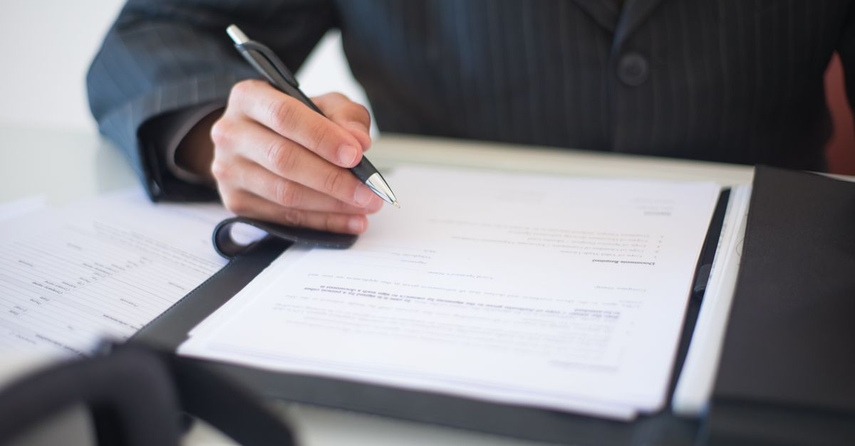 Close-up of a hand signing documents with a pen, symbolizing an important business contract.