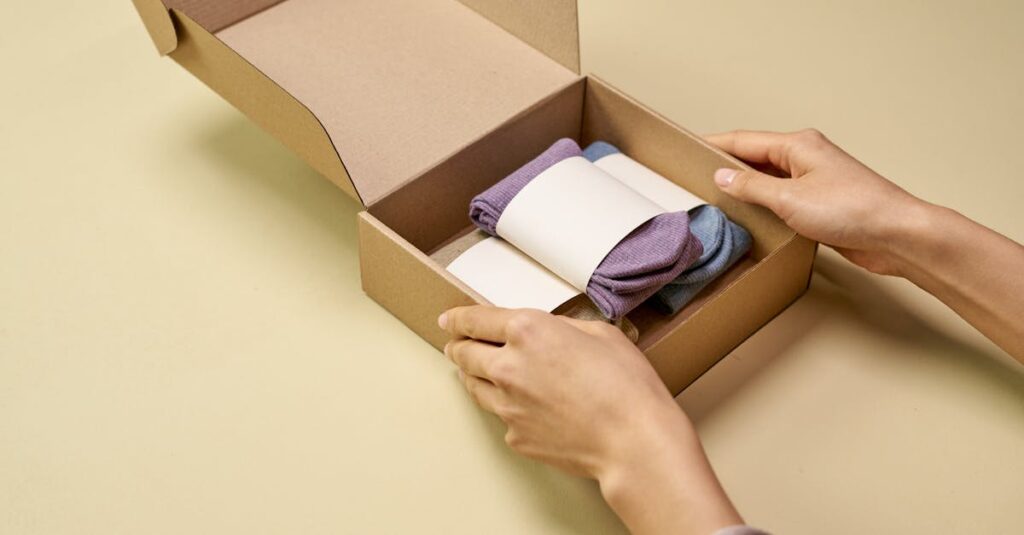 A person carefully places folded socks into a cardboard packaging box on a beige background.