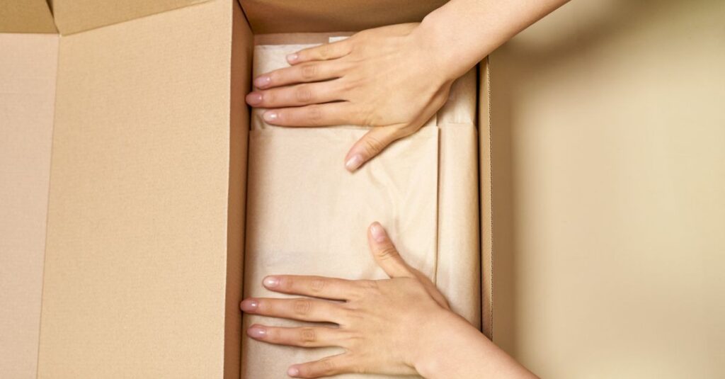 Close-up of hands packing a cardboard box with care using parchment paper.