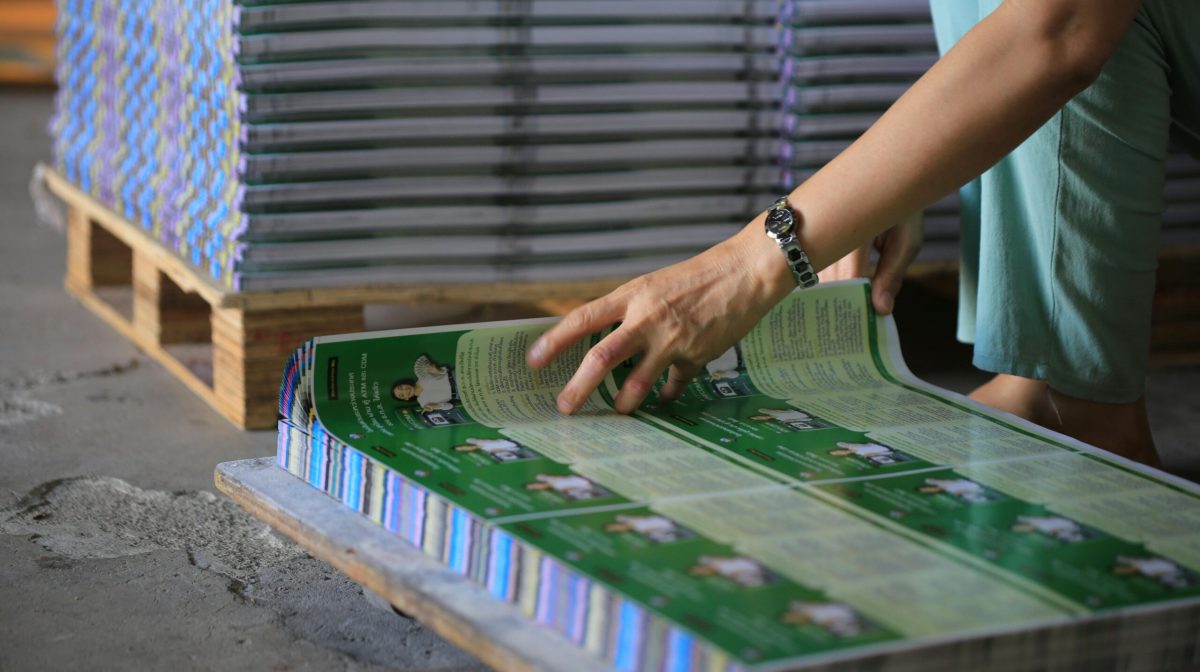 A person organizes stacks of printed publications in an industrial warehouse setting.